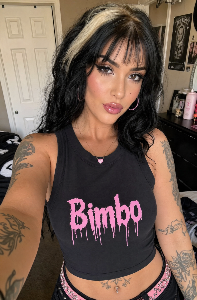 Black Bimbo racerback tank with pink graffiti print, worn by a dark-haired model in a bedroom.