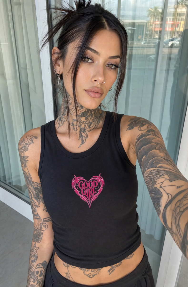 Black Good Girl racerback tank with a pink tribal heart graphic, worn by a dark-haired model by a window.