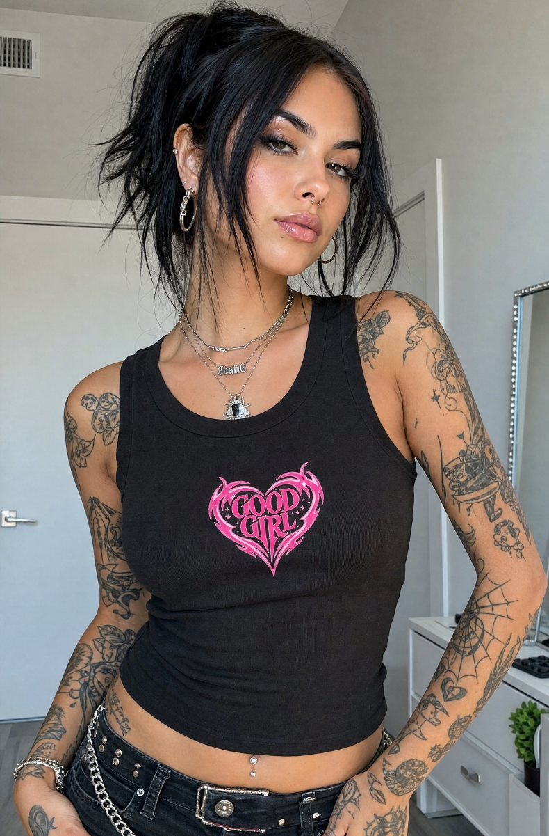 Black Good Girl racerback tank with a pink tribal heart graphic, worn by a dark-haired model in a bedroom.