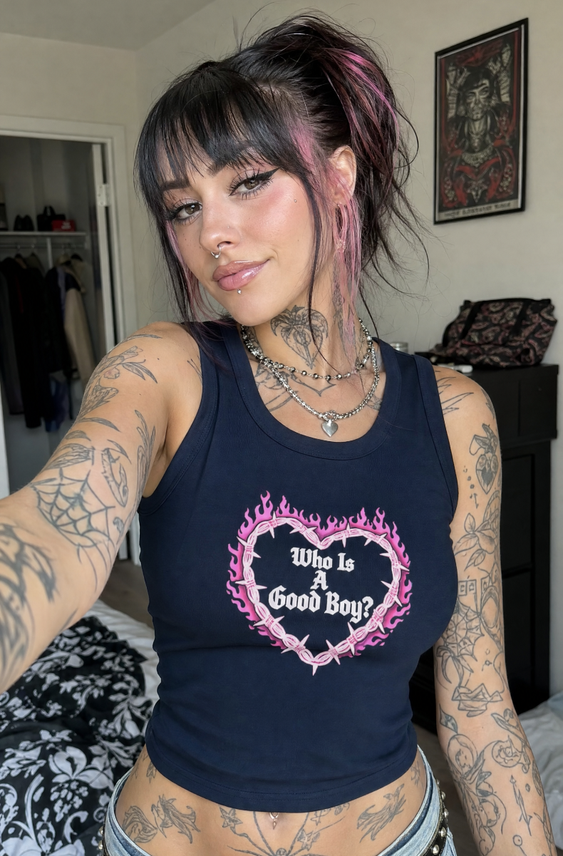 Navy Who Is A Good Boy racerback tank with a pink flaming barbed-wire heart graphic, worn by a model in a bedroom.