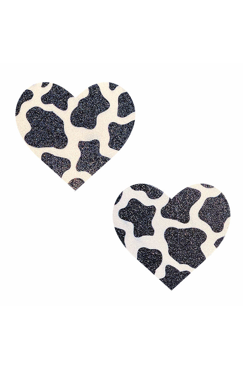 Two heart-shaped pasties in cow print: a white-glitter base with irregular black-glitter spots scattered across each.