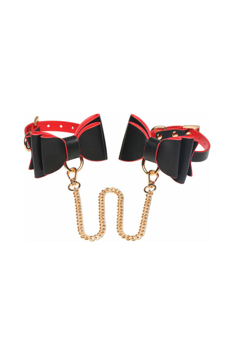 Two black bow cuffs joined by a long gold chain connector, on white.