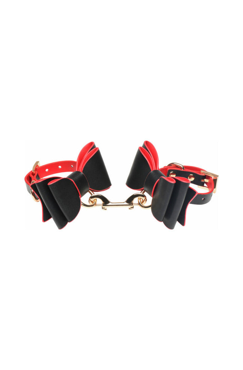 Two black bow cuffs joined by a short gold double-snap-hook connector, on white.