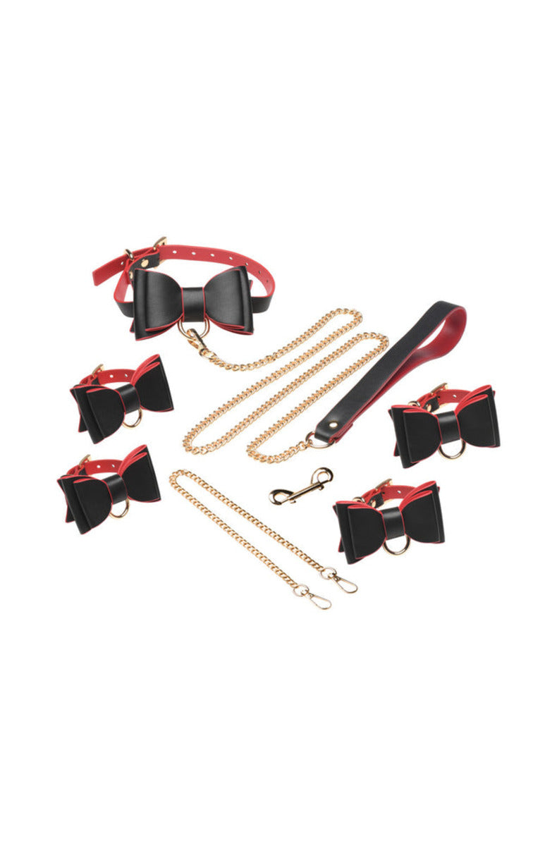 Black and red vegan leather goth bondage set laid out: bow collar, gold chain leash, wrist and ankle cuffs, and connectors.