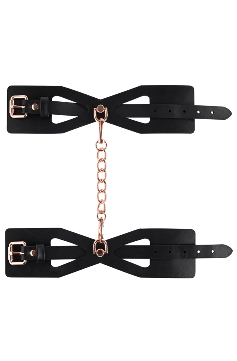 Flat layout of two black corset-cutout wrist cuffs joined by a rose-gold chain on a white background.