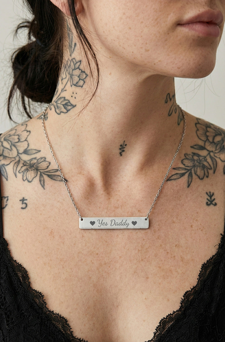 Necklace with a 'yes daddy' bar pendant worn by a person with tattoos on their neck and shoulders.