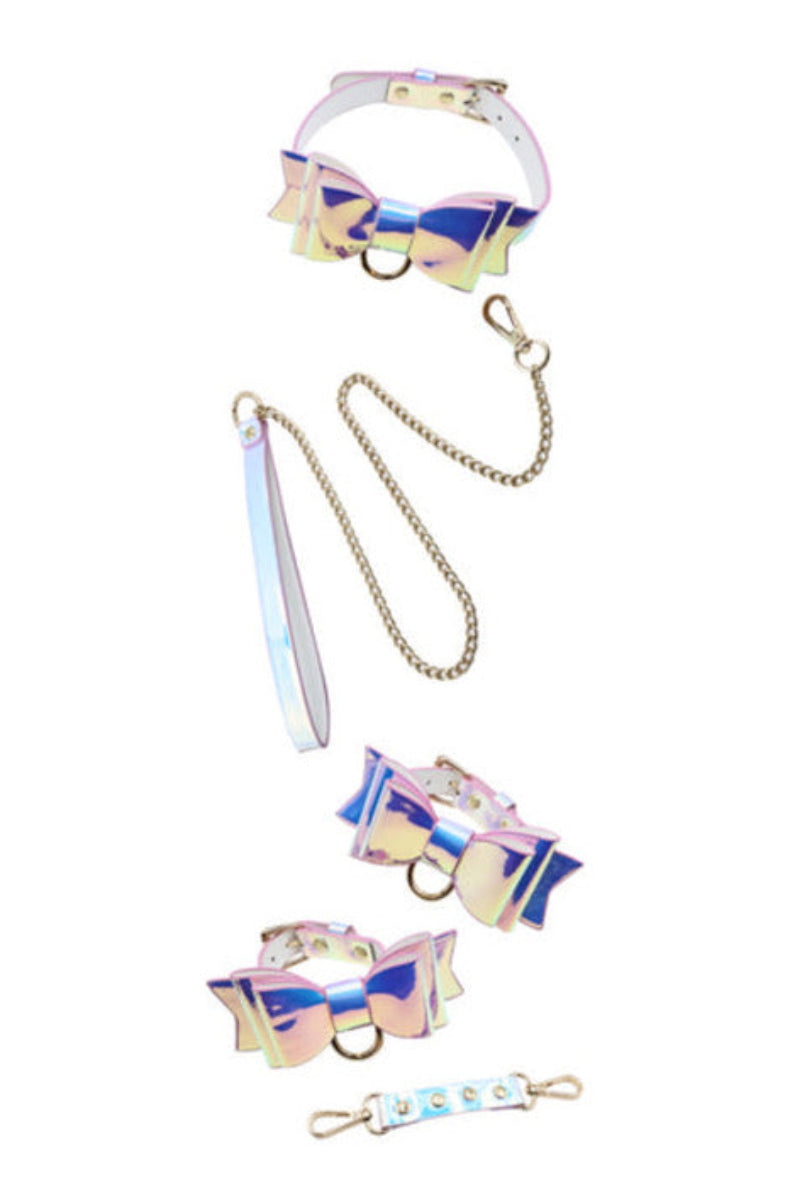 Flat lay of the iridescent pastel fairy bondage set: bow collar, leash, two bow cuffs, and a studded connector, on white.