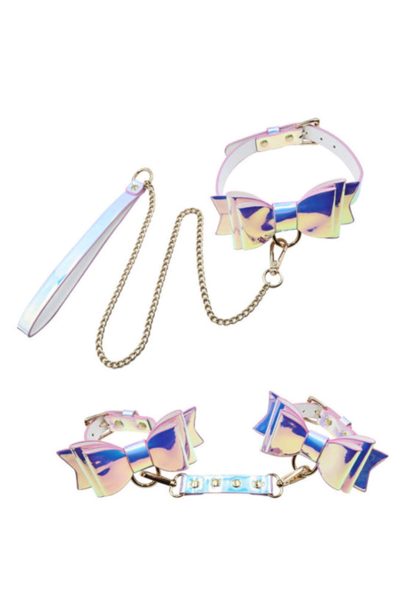 Iridescent pastel fairy bondage set flat lay: bow collar, gold chain leash, and two bow cuffs joined by a connector.