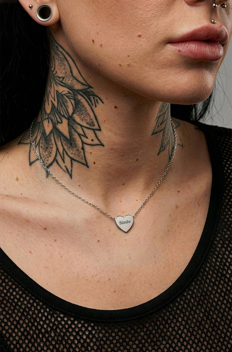 Silver Bimbo heart necklace on tattooed model wearing black mesh top with tunnel ear jewelry
