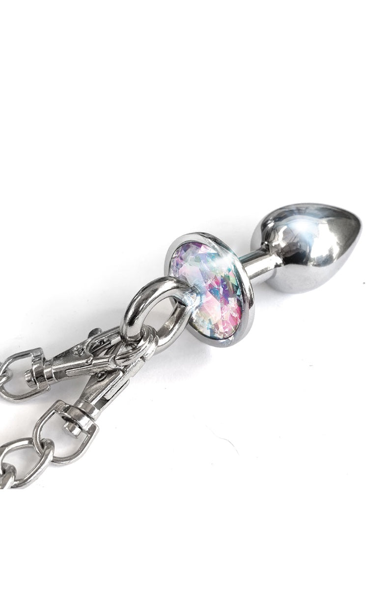 Close-up of chrome butt plug with iridescent jewel base attached to silver chain with handcuff visible