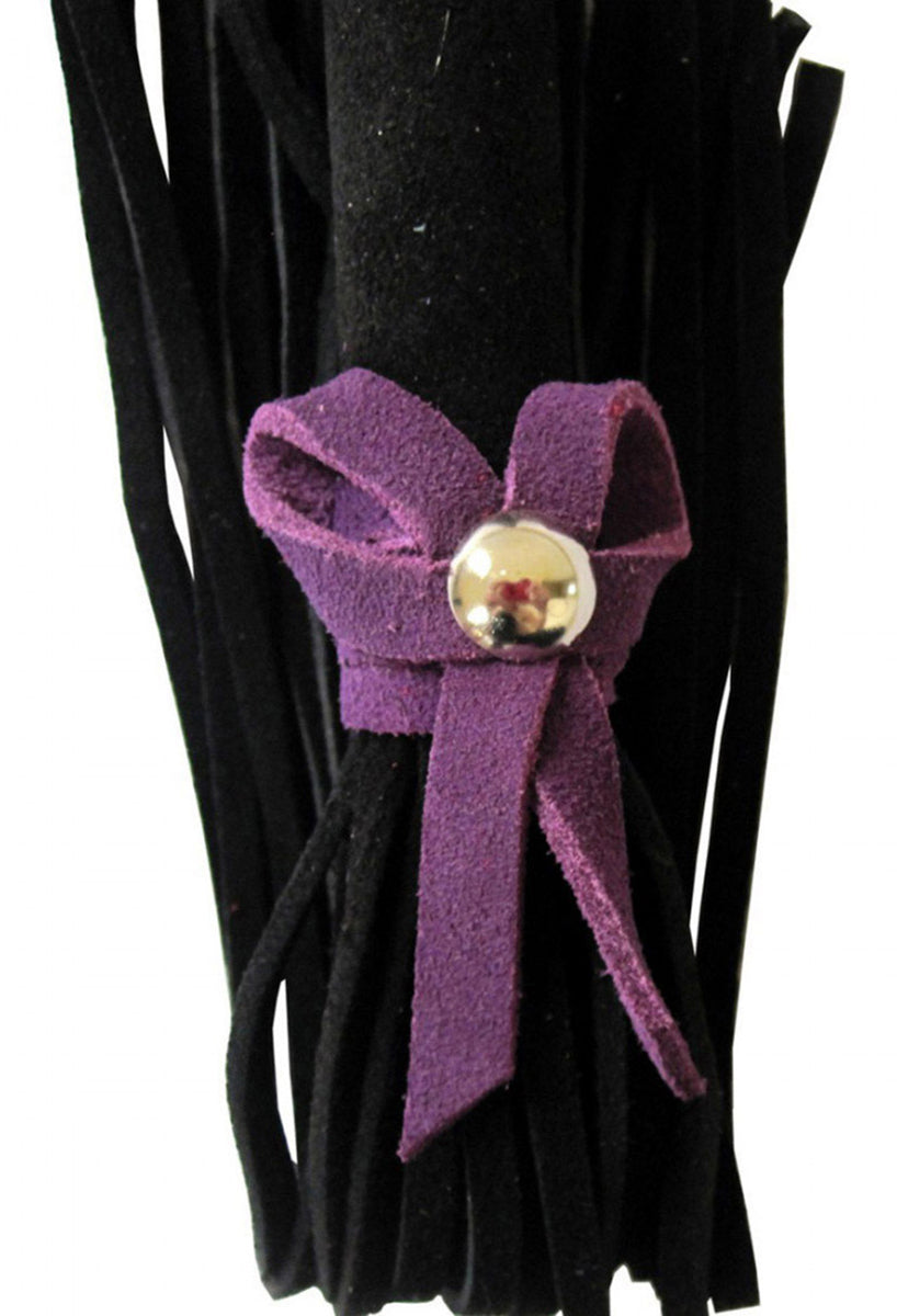 Detail view of the purple suede bow with a silver dome stud tied around the black suede falls of the mini flogger.