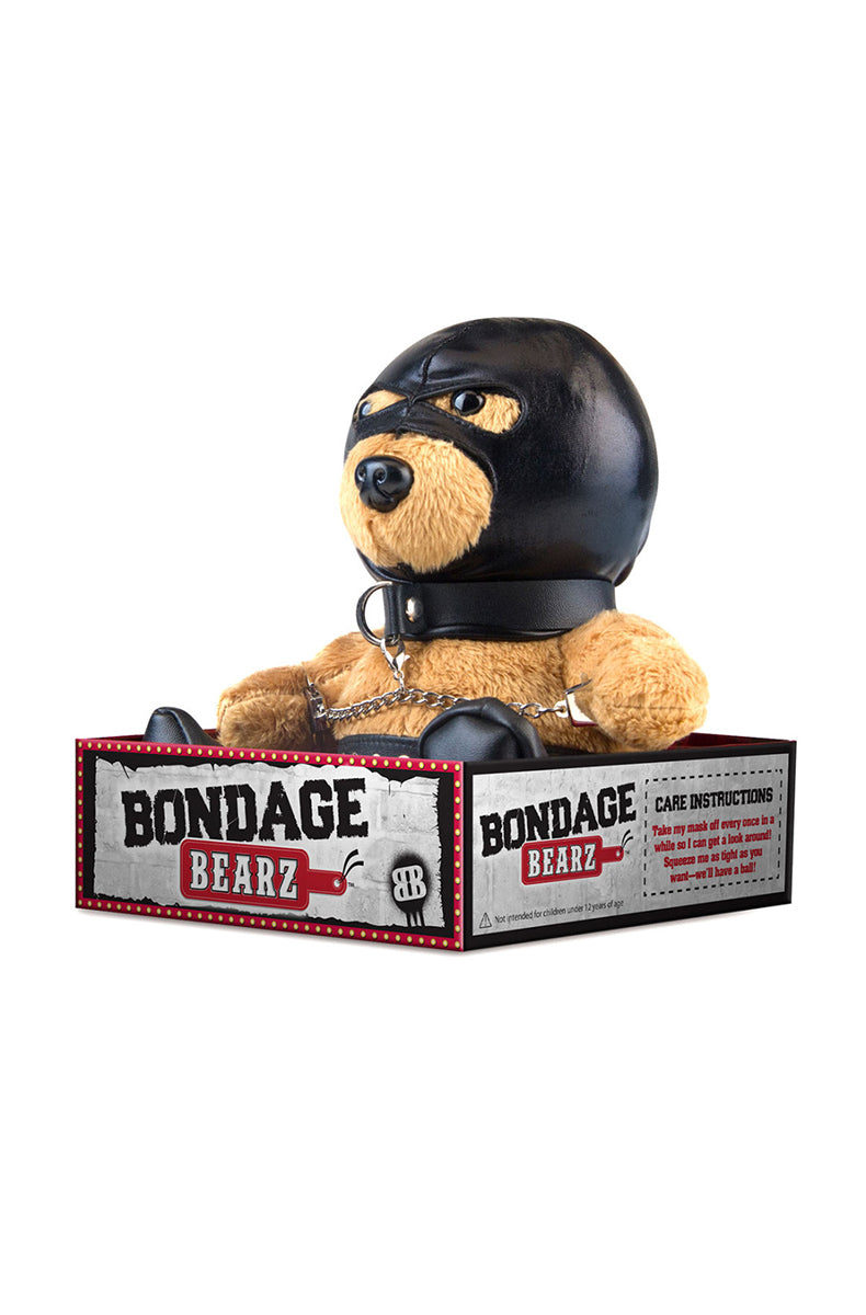 Side view of tan plush teddy bear showing black faux leather hood, collar chain, and silver-studded panties.