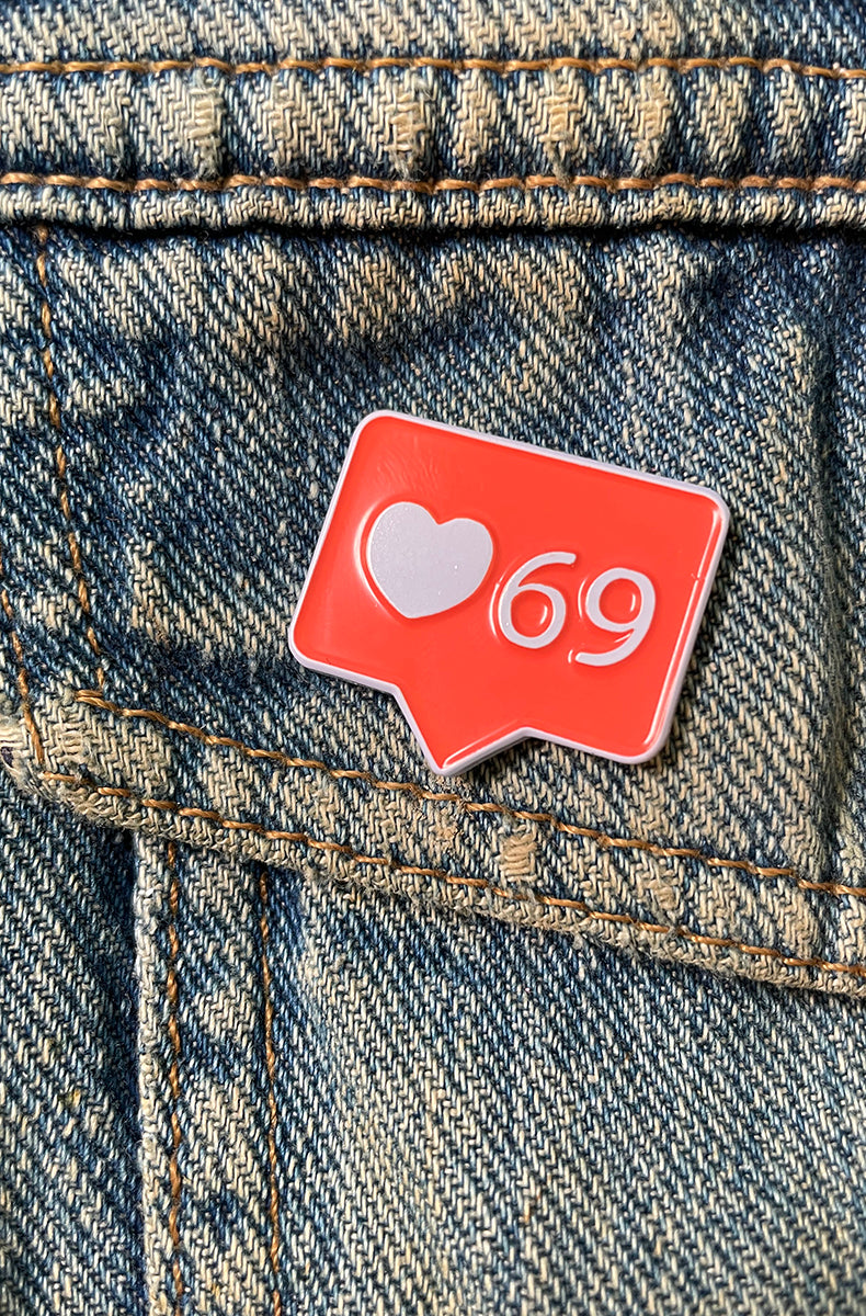 Red speech-bubble enamel pin shaped like a notification badge, holding a white heart icon and the number 69.