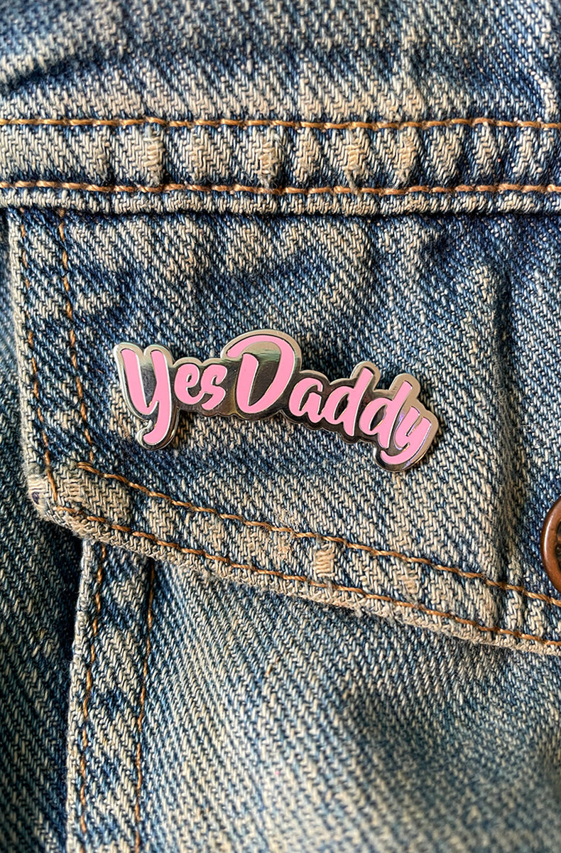 Pastel-pink enamel pin shaped to follow the cursive words "Yes Daddy" with a polished silver outline.