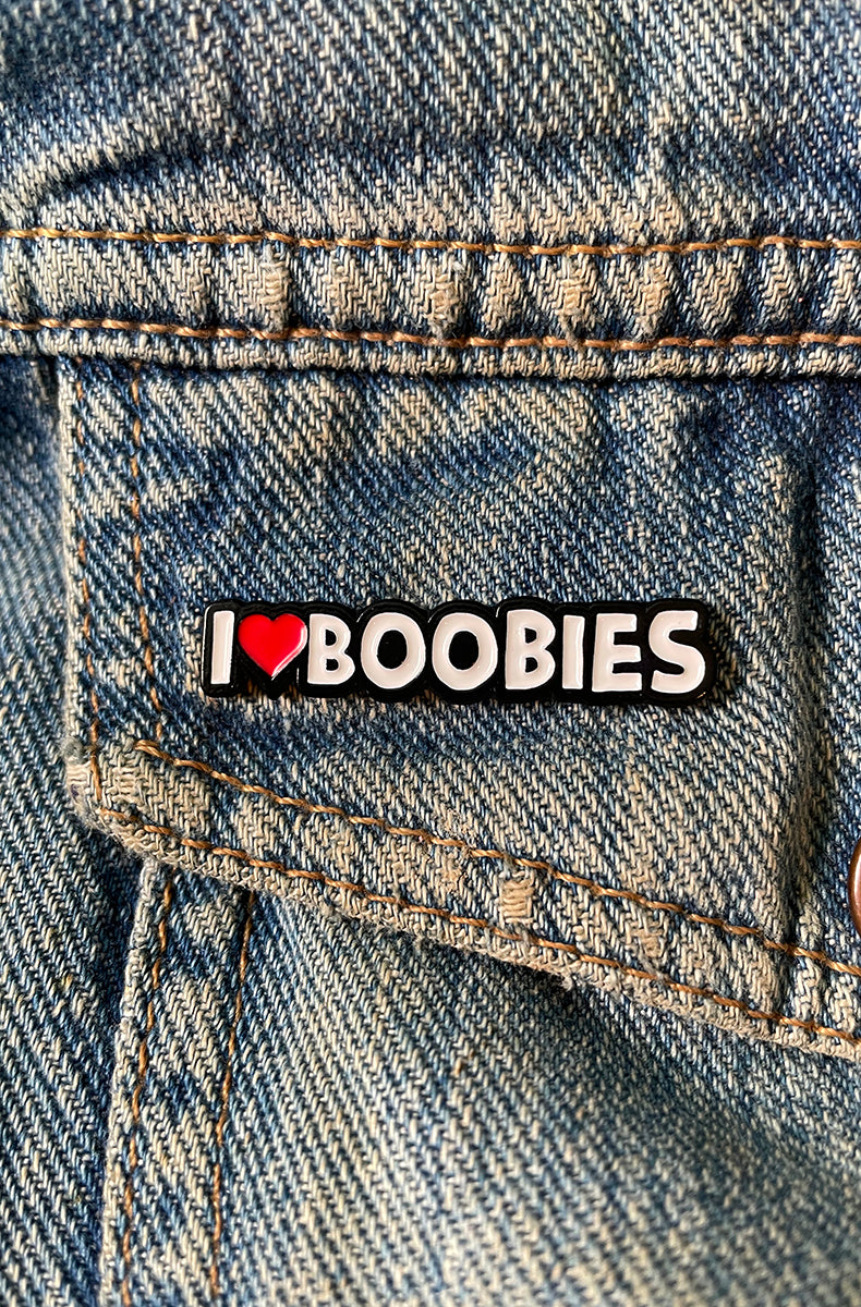 Slim black enamel pin reading I, a small red heart, and BOOBIES in white block letters with a silver outline.