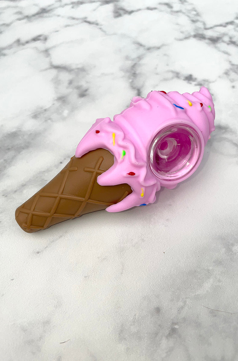 Three PIECEMAKER ice cream cone silicone pipes in yellow, purple, and pink with sprinkle accents and glass bowls, on marble.
