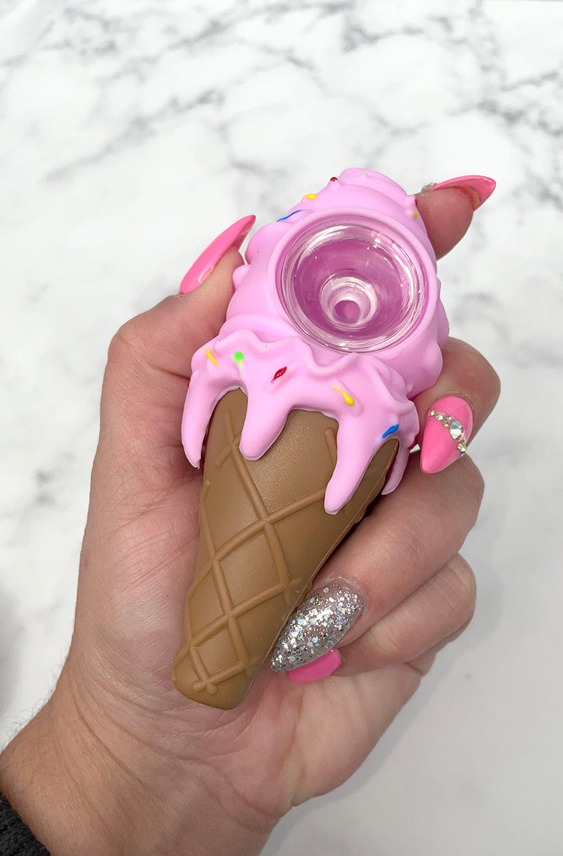 Three PIECEMAKER ice cream cone silicone pipes in yellow, purple, and pink with sprinkle accents and glass bowls, on marble.