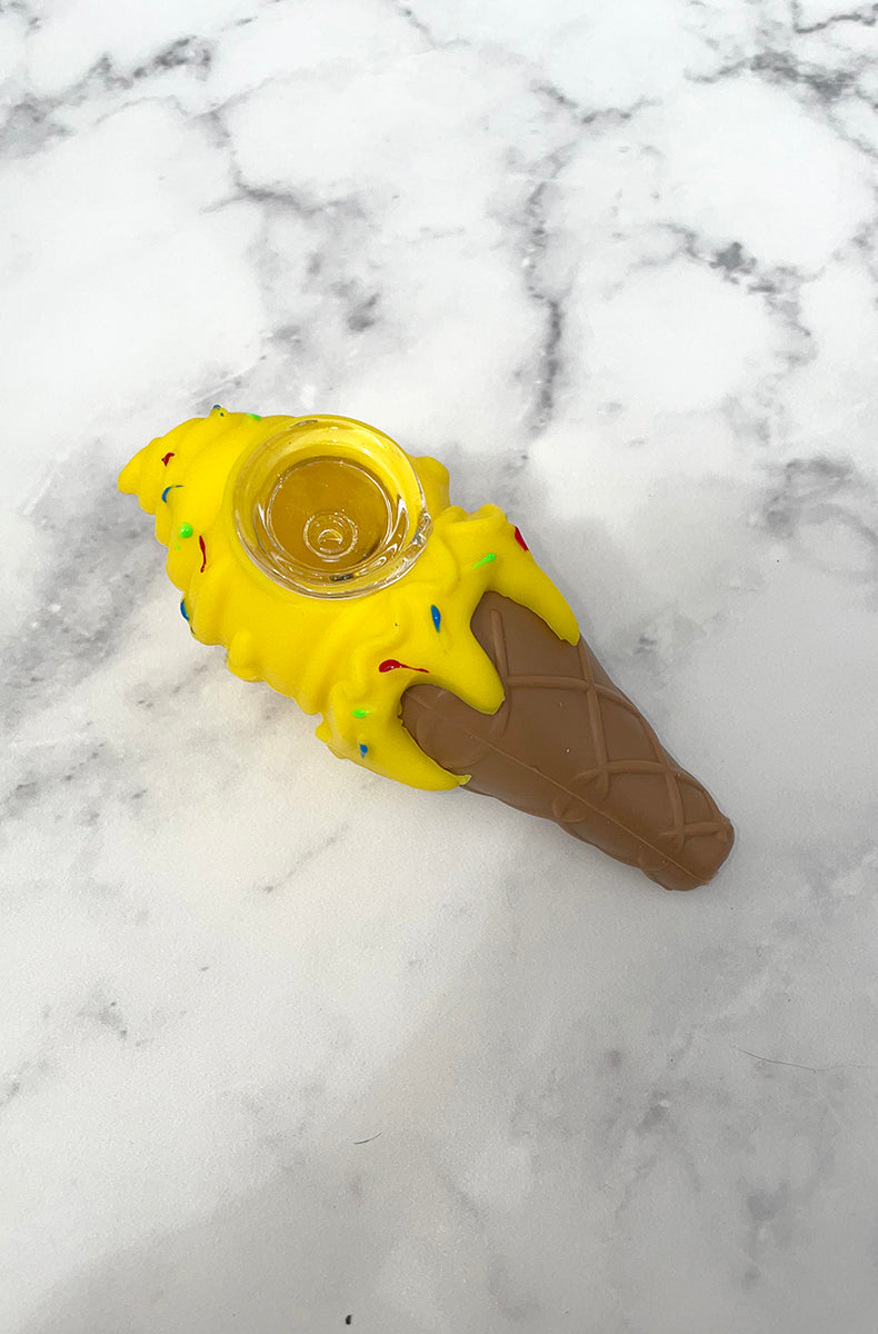 Three PIECEMAKER ice cream cone silicone pipes in yellow, purple, and pink with sprinkle accents and glass bowls, on marble.