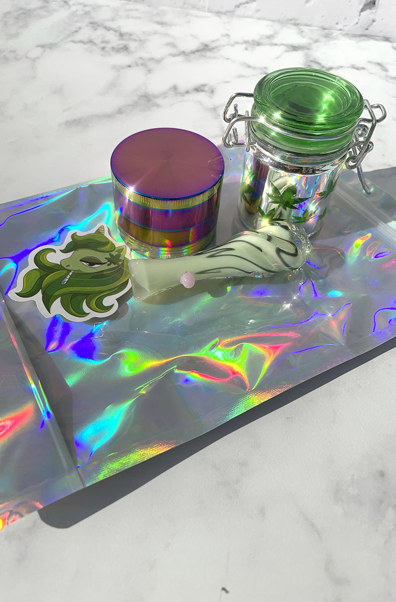 Stash starter pack on holographic pouch: glass swirl chillum, glass leaf jar, rainbow grinder, unicorn sticker.