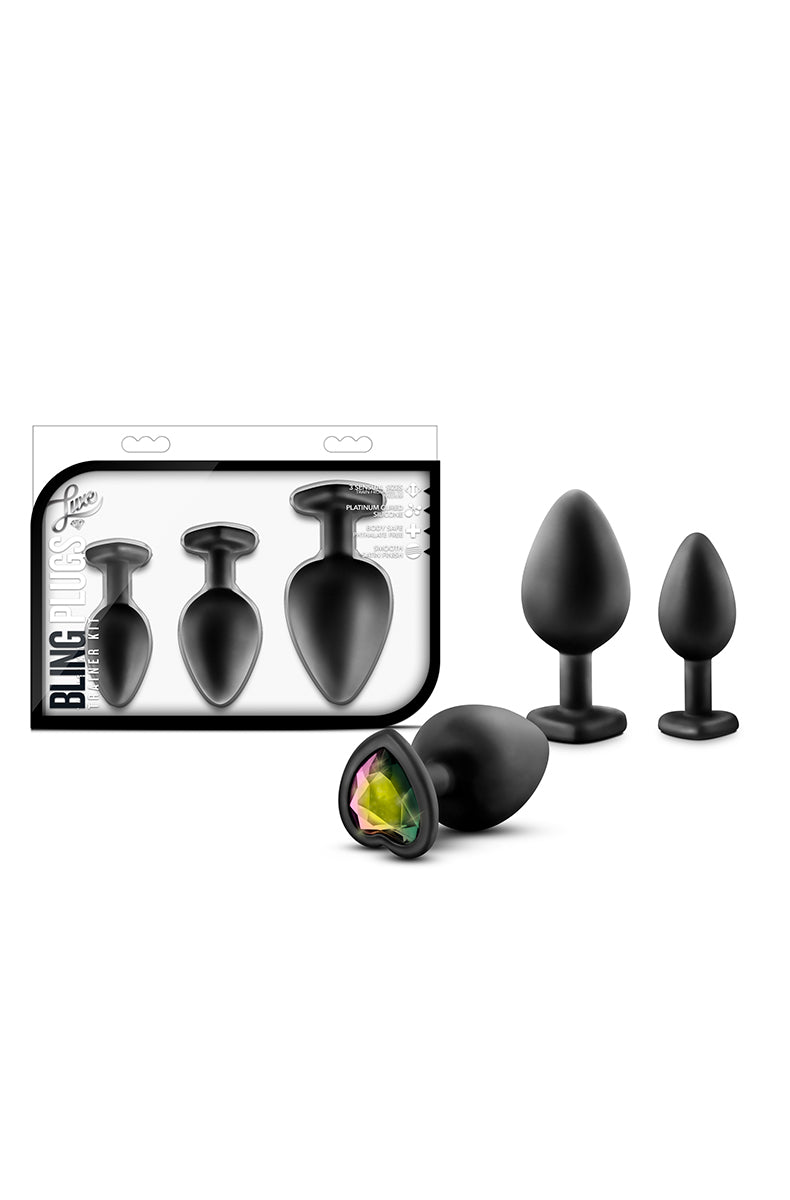 Three matte black silicone anal plugs with iridescent heart gem bases, beside the Bling Plugs Trainer Kit package.