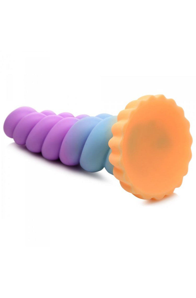 Pastel unicorn silicone dildo shown stuck via suction cup base to a flat surface.