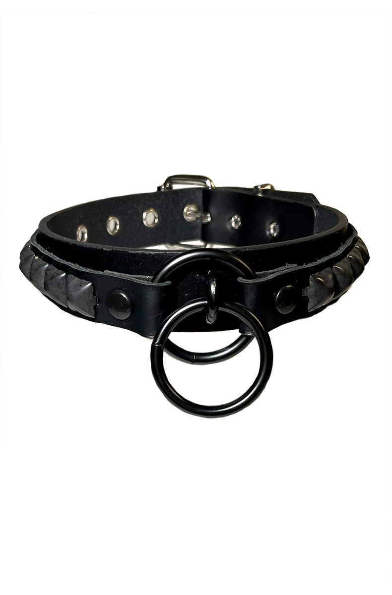 Black vegan-leather collar with woven leather edge trim along the top and bottom and twin black metal O-rings at the front center.