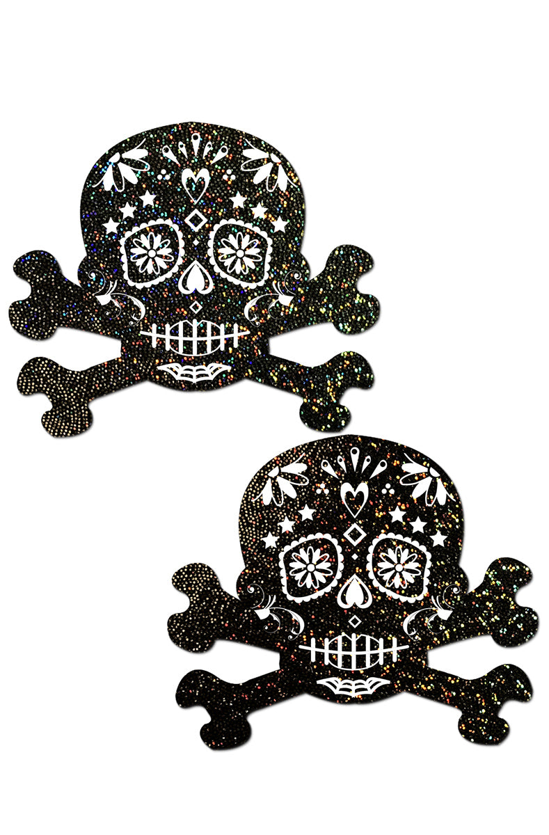 Two sugar-skull-and-crossbones pasties in black holographic glitter with white Day-of-the-Dead floral, heart, daisy-eye, and stitched-mouth detailing.