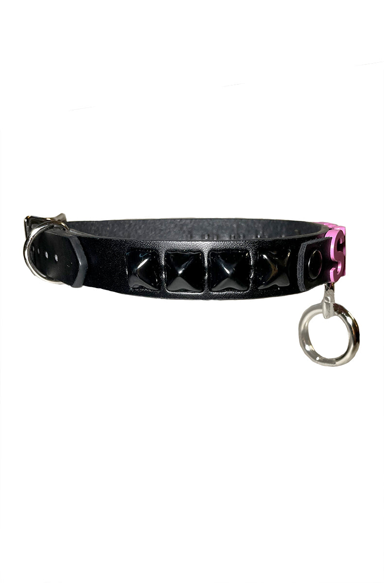 Black vegan leather collar with raised pink SLUT lettering, black pyramid studs, and a silver D-ring with attached O-ring at the front.