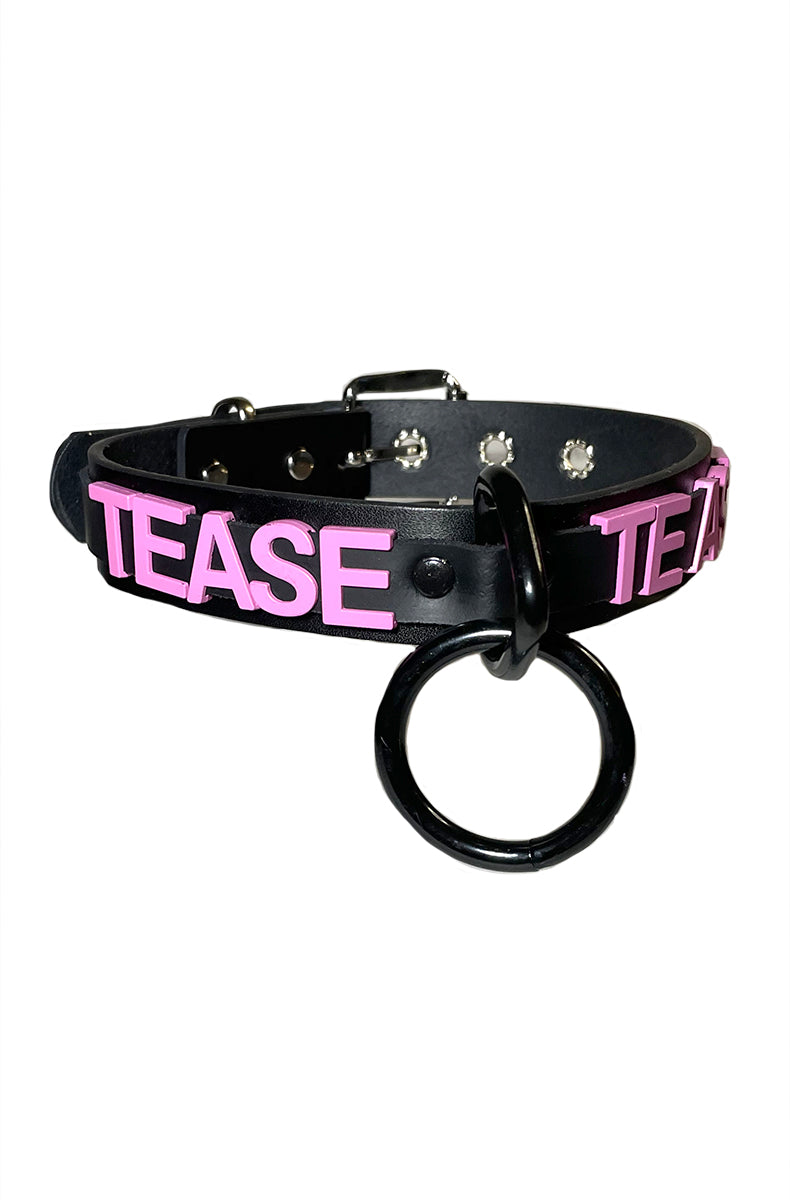 Black vegan leather collar with raised pink TEASE lettering and a large black O-ring suspended from a black D-ring at the front.