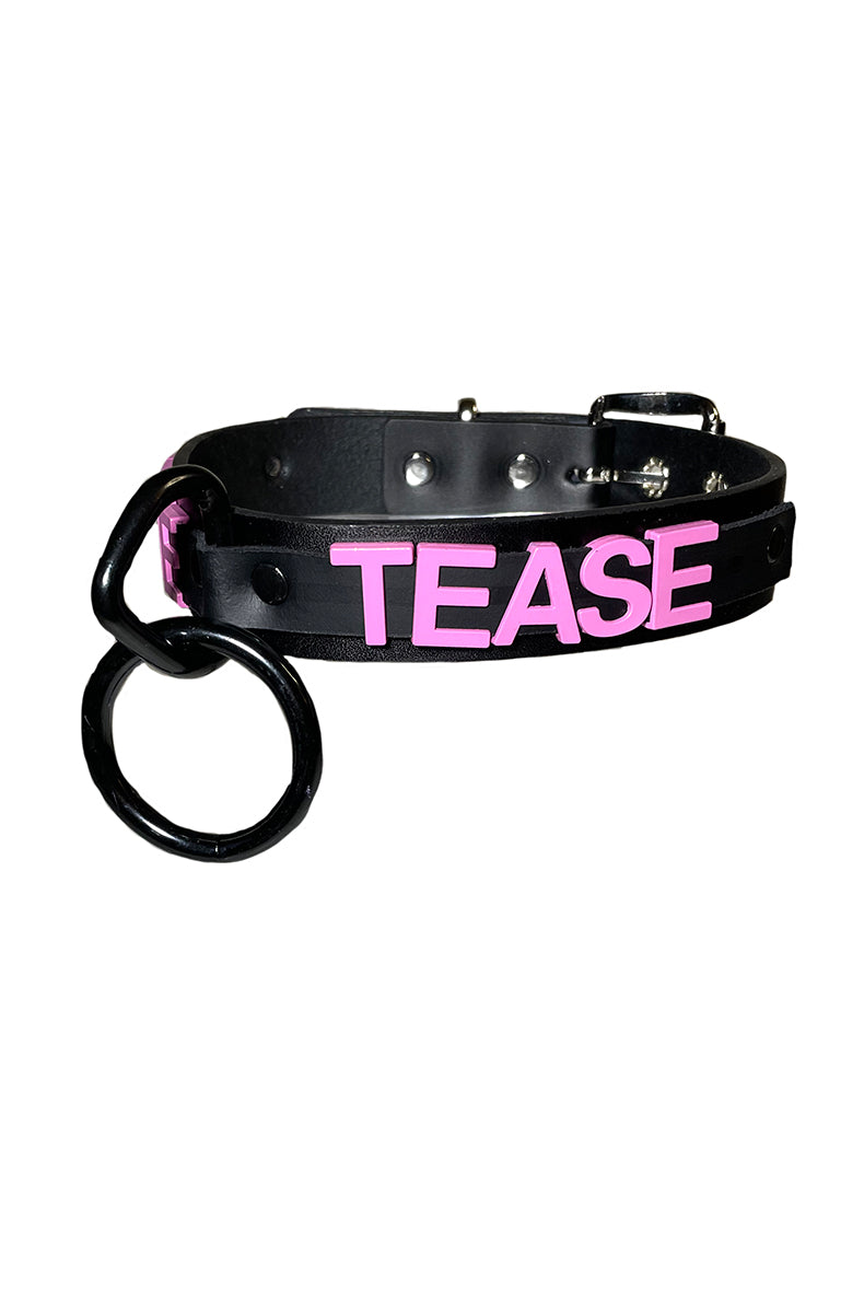 Black vegan leather collar with raised pink TEASE lettering and a large black O-ring suspended from a black D-ring at the front.